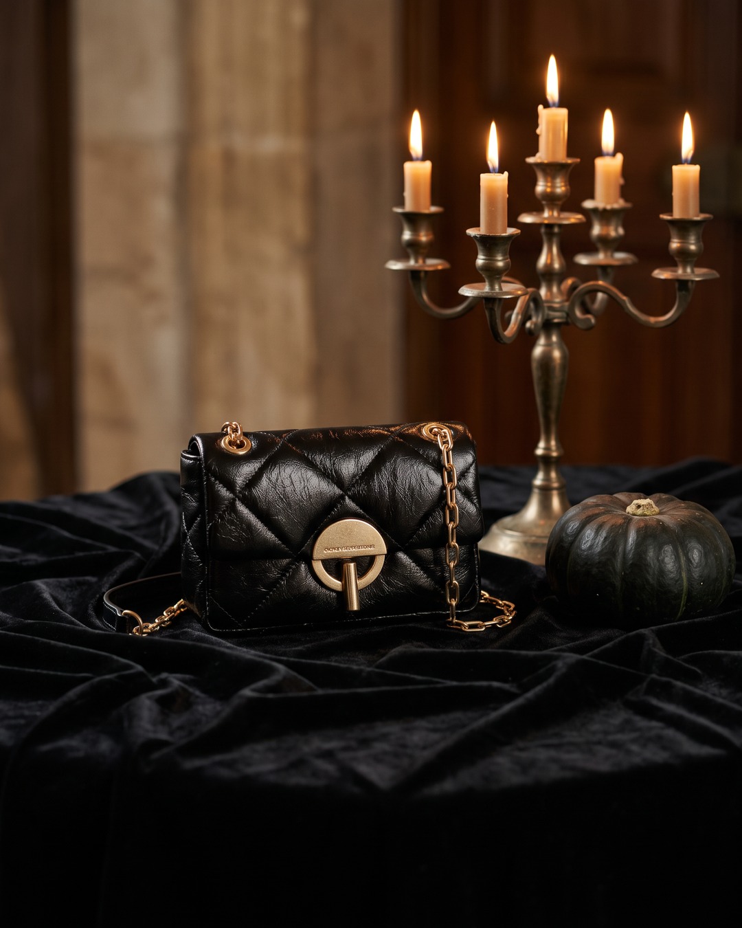 Bolso negro acolchado con broche dorado sobre terciopelo y velas